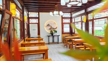 A traditional wooden interior with tables and benches, a central decorative wall, and large windows.