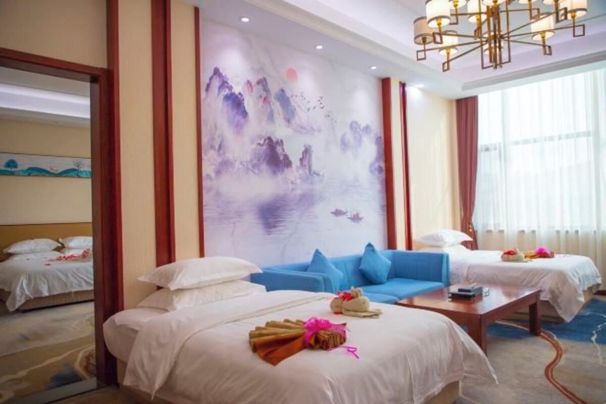 Ein Hotelzimmer mit zwei Betten, einem blauen Sofa, einem Holztisch und einem großen Wandbild.