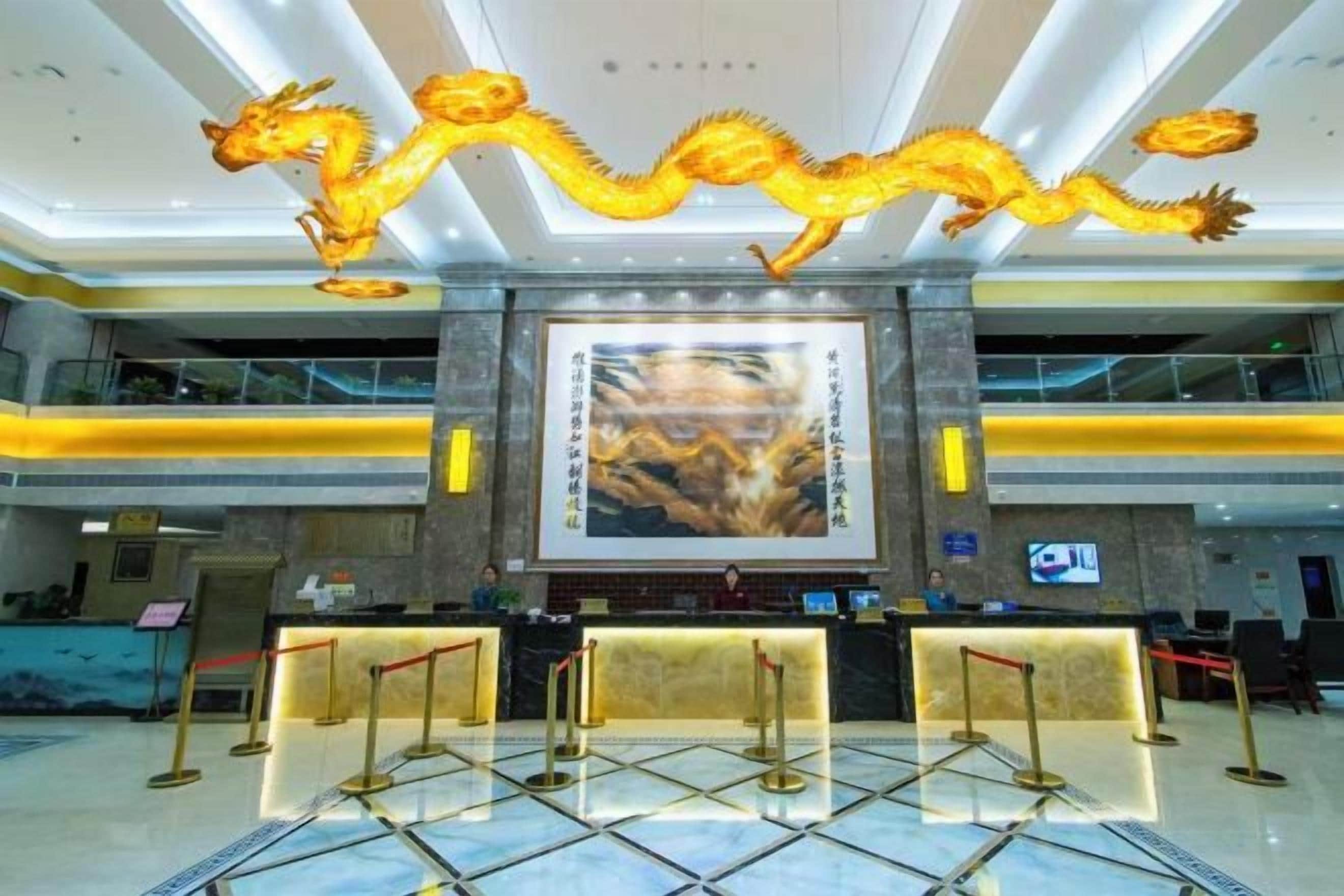 A hotel lobby with a reception desk, a large dragon decoration, and a prominent poster on the wall.