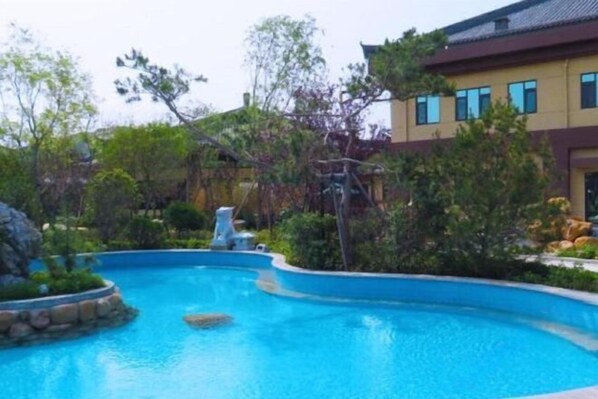 Una piscina rodeada de exuberante vegetación y un edificio moderno con tejado de baldosas.