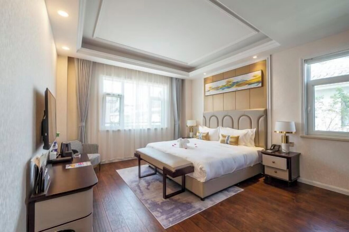 A modern hotel room with a large bed, bedside tables, a desk, and a TV.