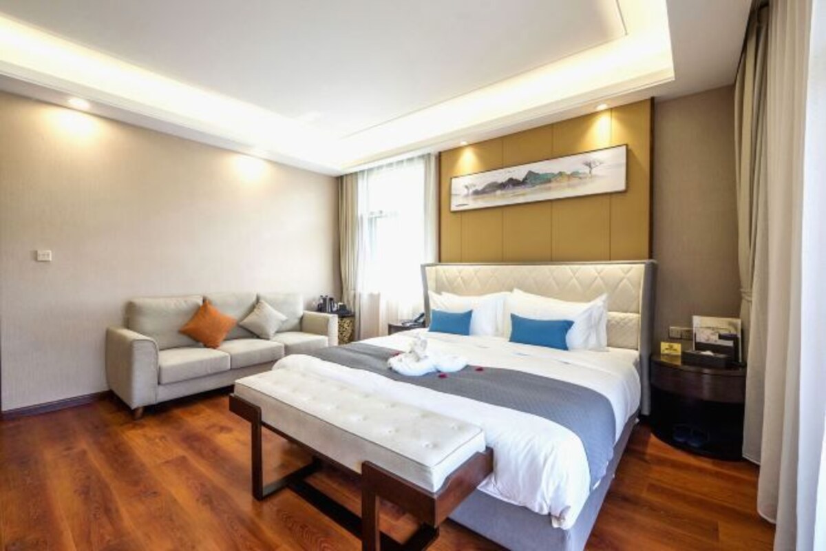 Ein Hotelzimmer mit einem großen Bett, einer Couch, einer Bank und einem Bild an der Wand.
