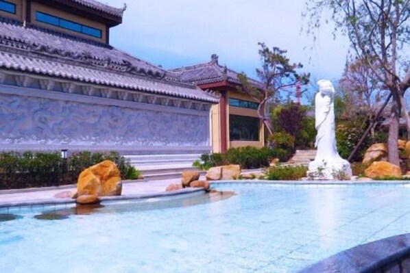 A traditional building with a tiled roof, a stone pathway, and a water feature with a statue.