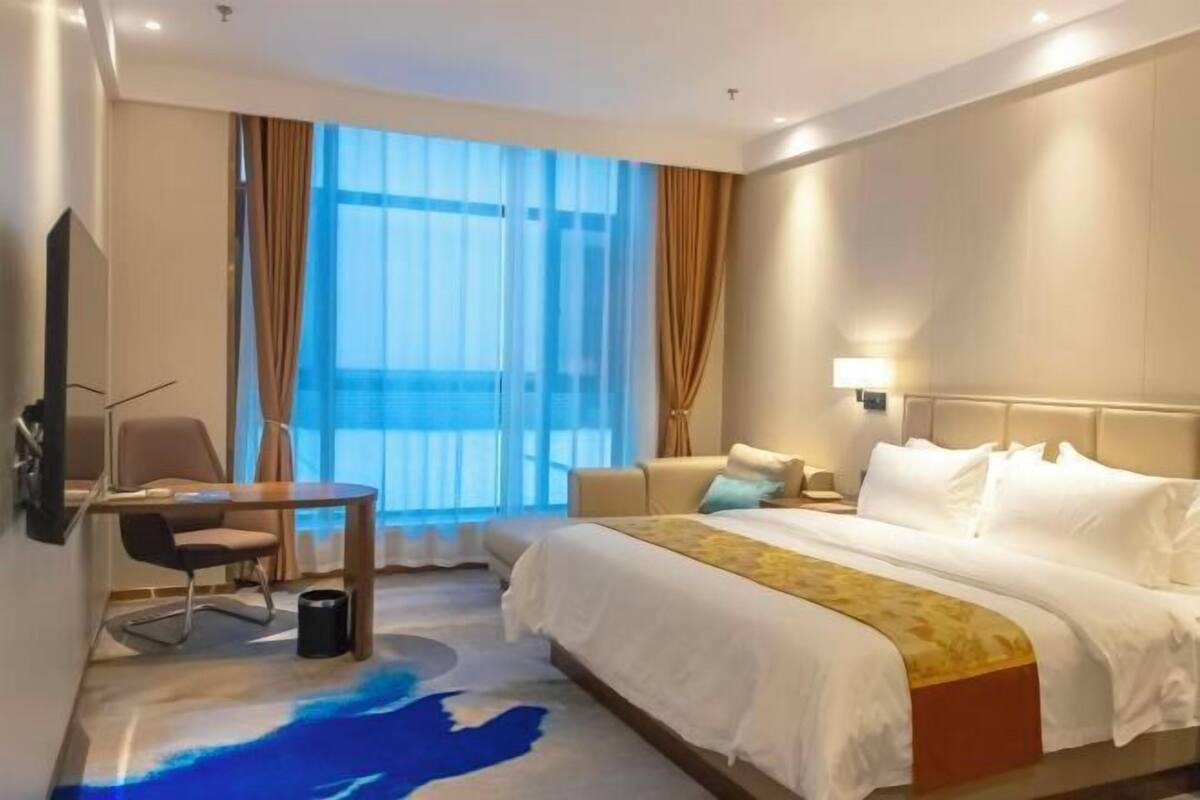 A hotel room with a bed, a desk, a chair, a TV, and a window with curtains.