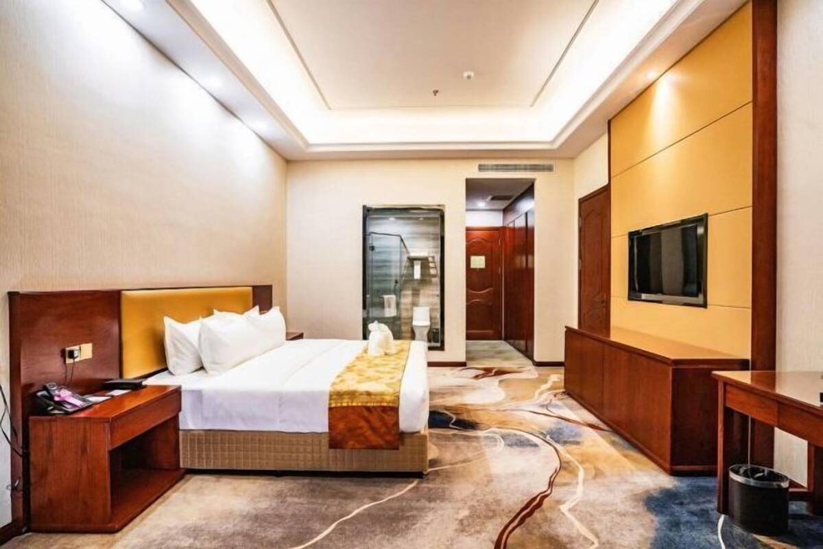 A hotel room with a bed, bedside table, TV, and a carpeted floor.