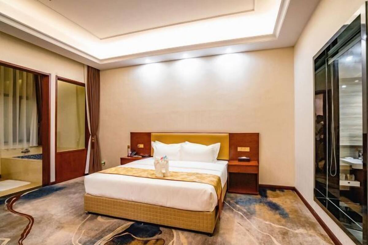 A hotel room with a bed, bedside tables, a mirror, a wardrobe, and a shower area.