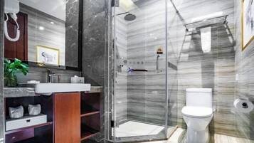 Un baño moderno con ducha envuelta en vidrio, inodoro blanco y tocador con encimera de mármol.