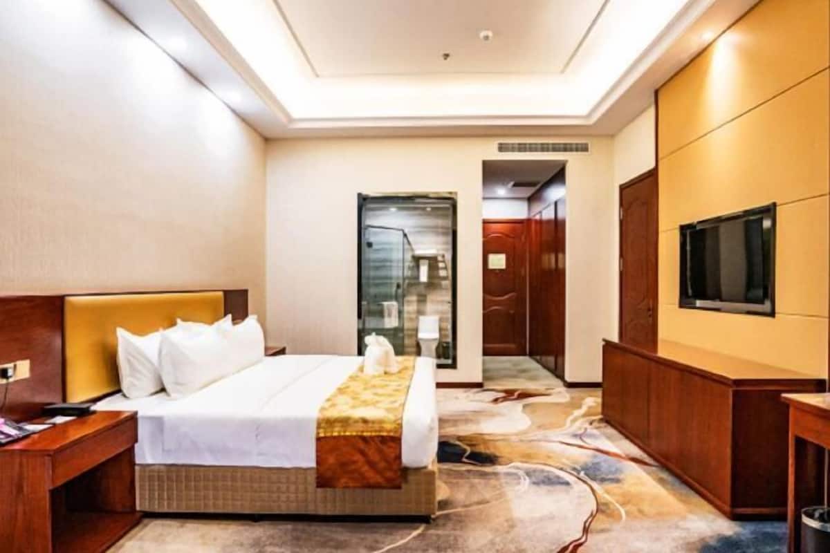 A hotel room with a bed, bedside table, TV, and a carpeted floor.