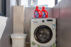 A compact, modern laundry room with a front-loading washing machine and two detergent bottles on top. - NAXI yage hotel (Lijiang)