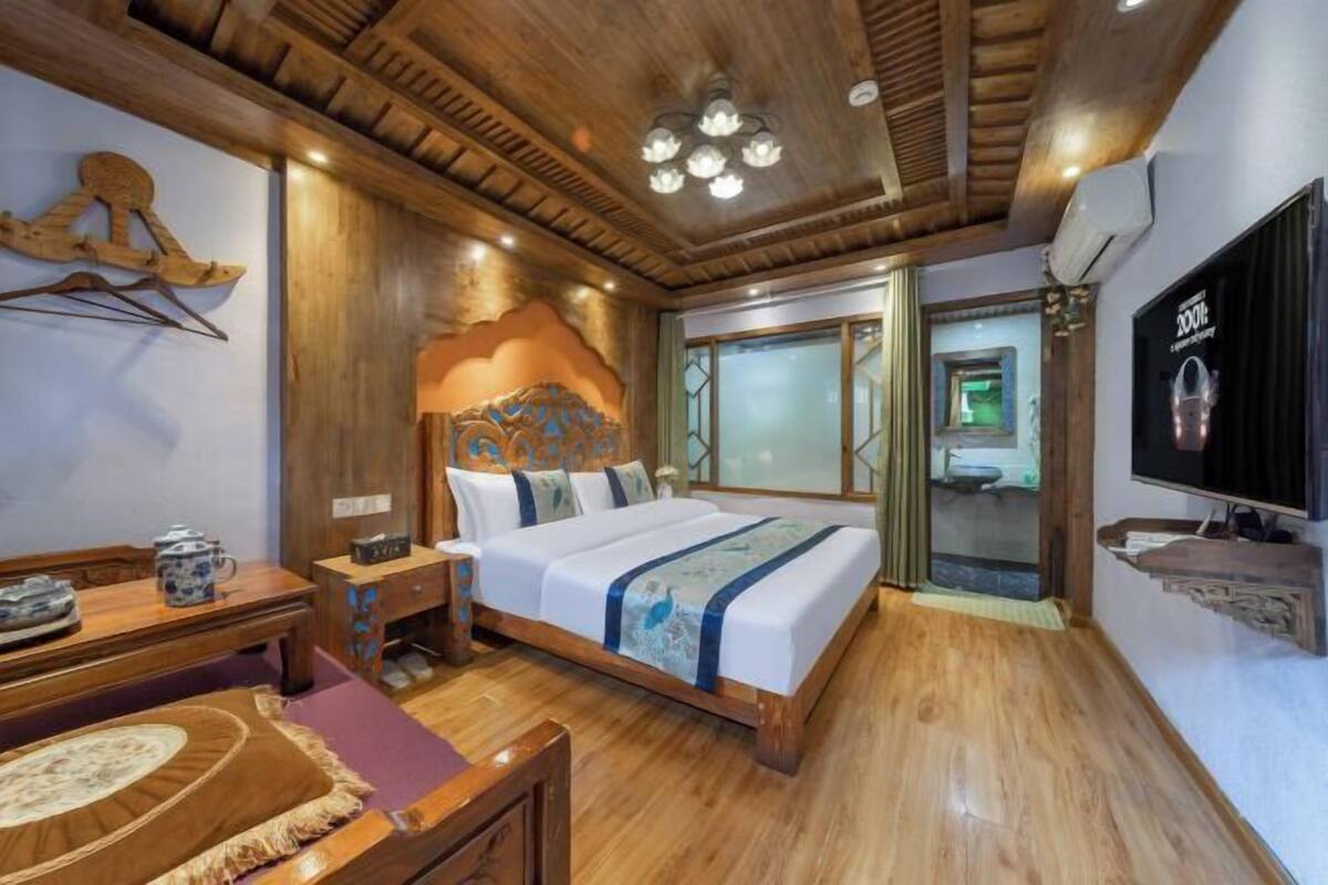 A wooden-floored room with a bed, a television, and a desk with a teapot.