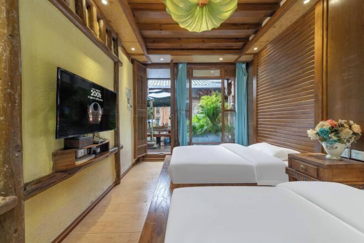 A hotel room with a television, two beds, a wooden ceiling, and a view of the outdoors.
