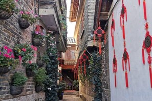 A narrow alleyway with brick buildings, hanging flower baskets, and red decorations. - NAXI yage hotel (Lijiang)