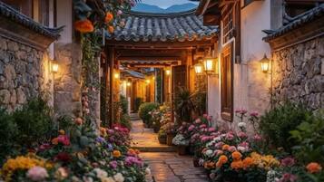 A traditional courtyard with stone walls, a tiled roof, and a pathway lined with potted flowers.