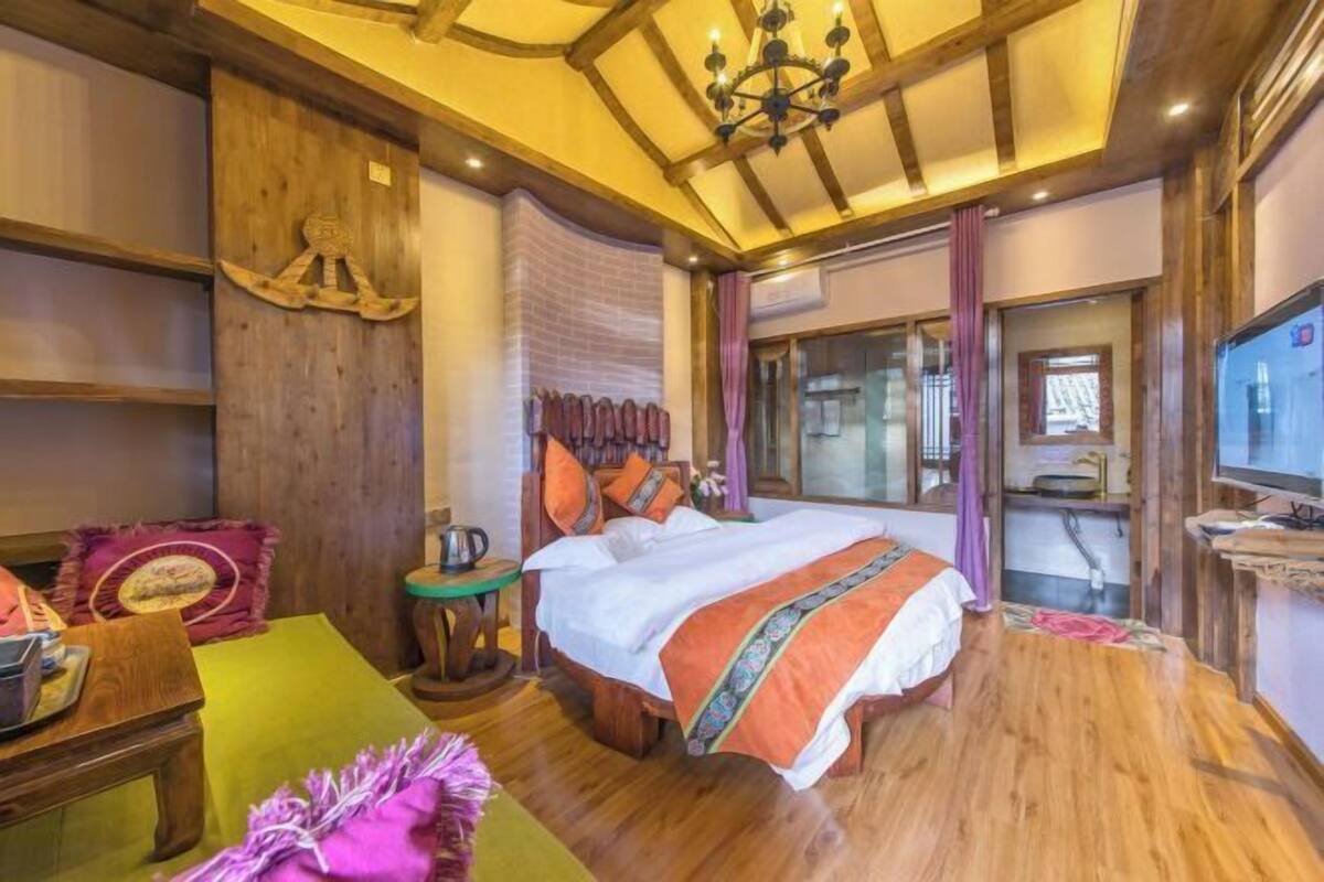A cozy bedroom with a wooden ceiling, a bed with a colorful blanket, a small table with a lamp, and a television on the wall.