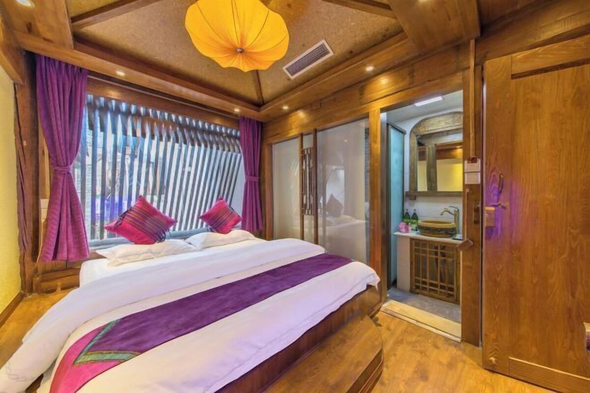 A bedroom with a large bed, wooden ceiling, and a bathroom with a sink and mirror.