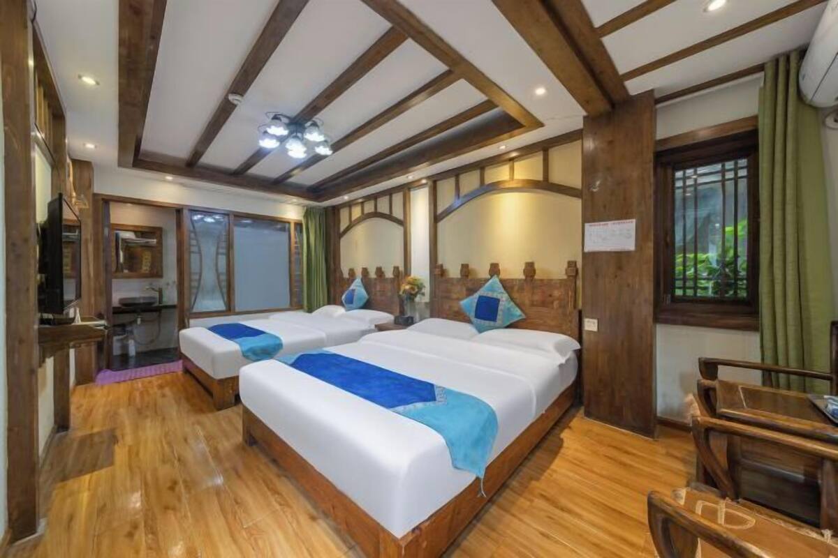 A hotel room with two beds, wooden flooring, a wooden ceiling, and a small dining area.
