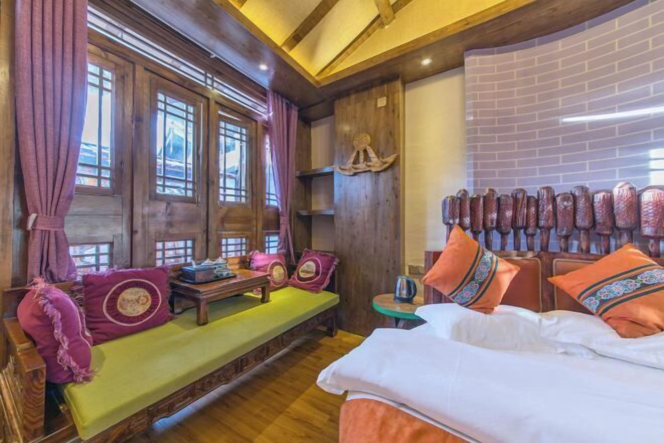 Ein gemütliches Zimmer mit einer hölzernen Bank, einem Bett mit bunten Kissen und einer Ziegelwand.