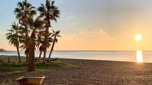 A beach with palm trees, a boat, and the sun setting over the ocean. - Nice apartment in Mijas with house sea view (Mijas)