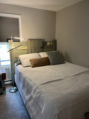 Une chambre à coucher avec un lit, une table de chevet, une lampe et une fenêtre avec des stores.