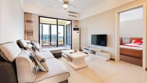 A modern living room with a sofa, TV, and a balcony view. - Sincerity Holiday Apartment Hostel (Haikou)