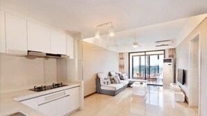 A modern kitchen with white cabinets, a built-in stove, and a dining area with a sofa and chairs. - Sincerity Holiday Apartment Hostel (Haikou)