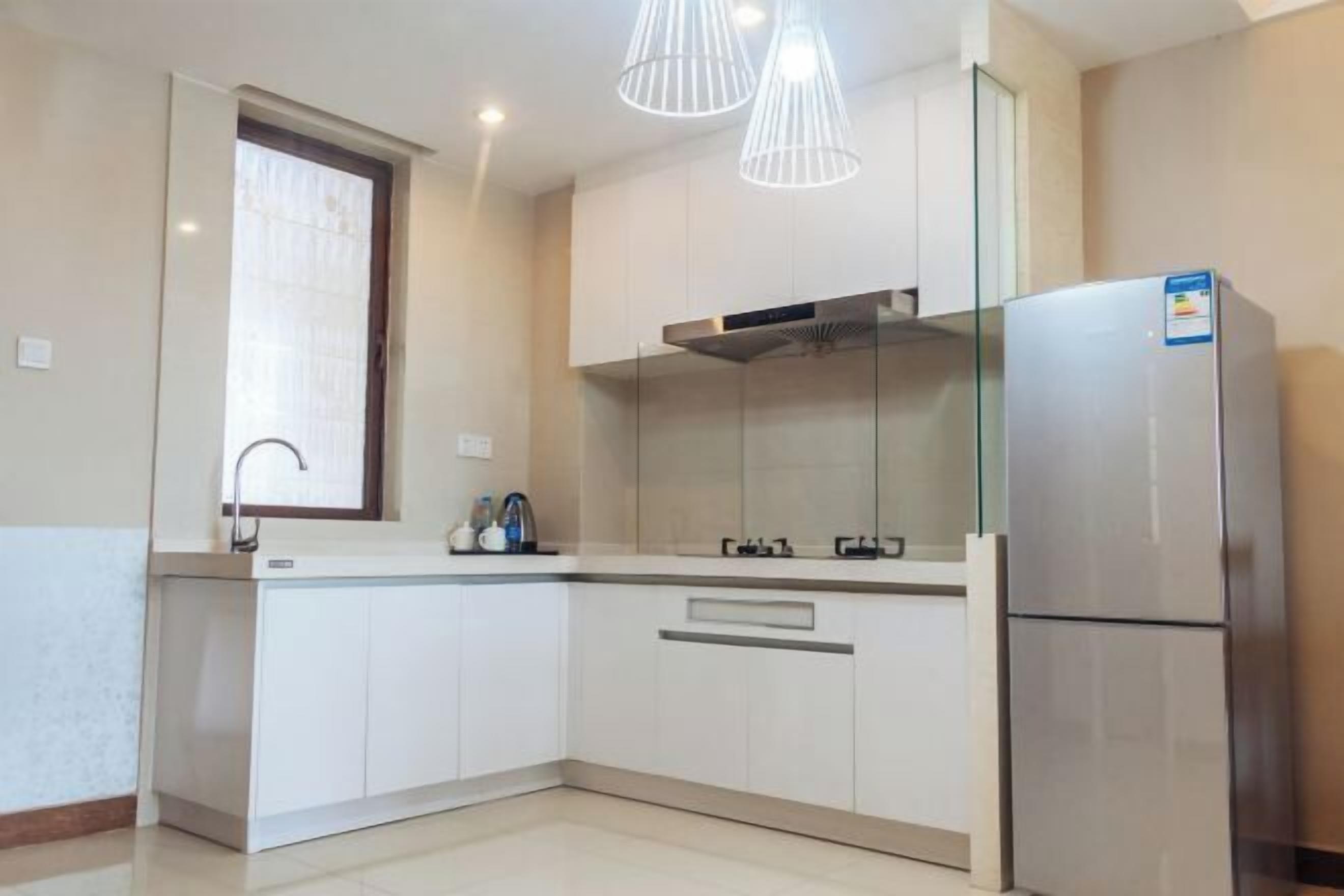 A modern kitchen with white cabinets, a stainless steel refrigerator, and pendant lighting.