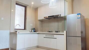 A modern kitchen with white cabinets, a stainless steel refrigerator, and pendant lighting.