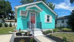 A single-story house with a front porch, a red door, and a small garden area with flowers and mulch. - NEW LISTING!!!  Villas Quaint Coastal Cottage short drive to Beaches (Lower Township)