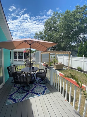 Um alpendre coberto com mesa e cadeiras, um guarda-sol decorativo e vista para o quintal.