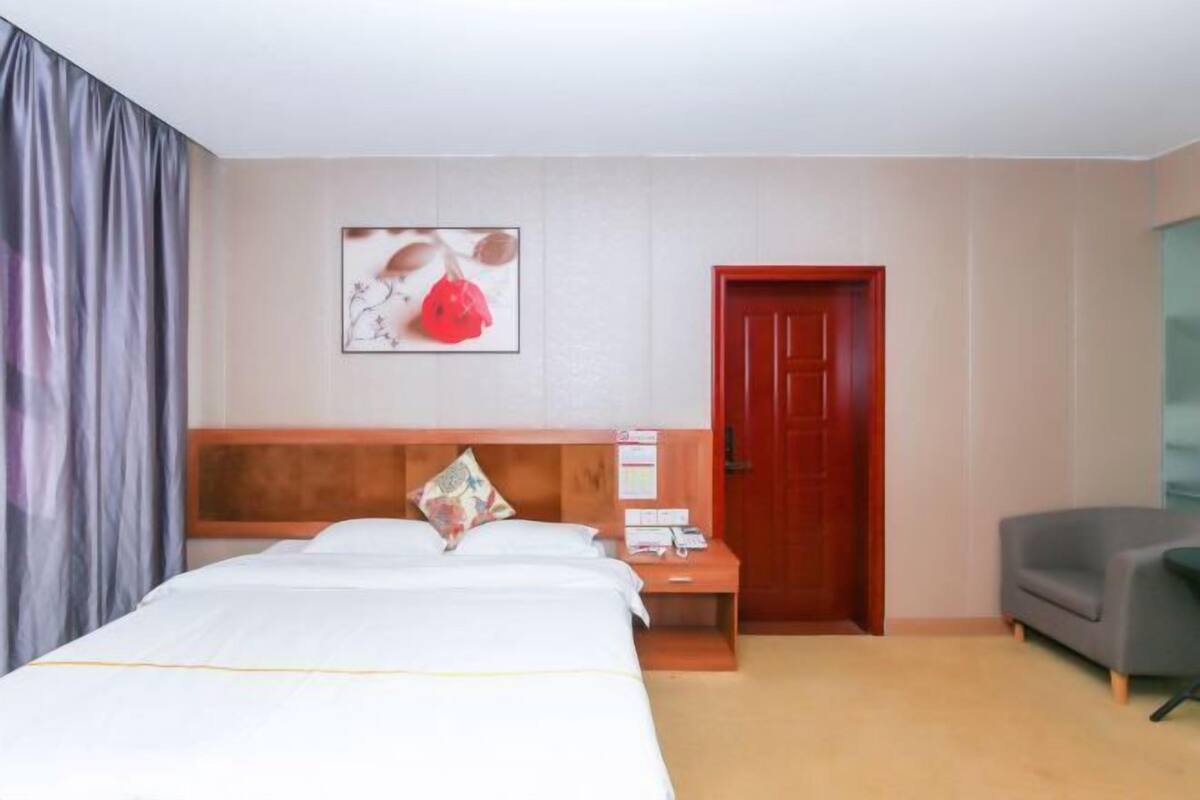 Ein Hotelzimmer mit Bett, Nachttisch, roter Tür und grauem Sessel.