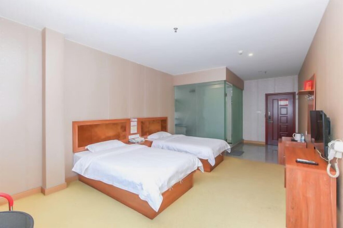 A hotel room with two beds, a desk with a telephone, and a glass shower enclosure.
