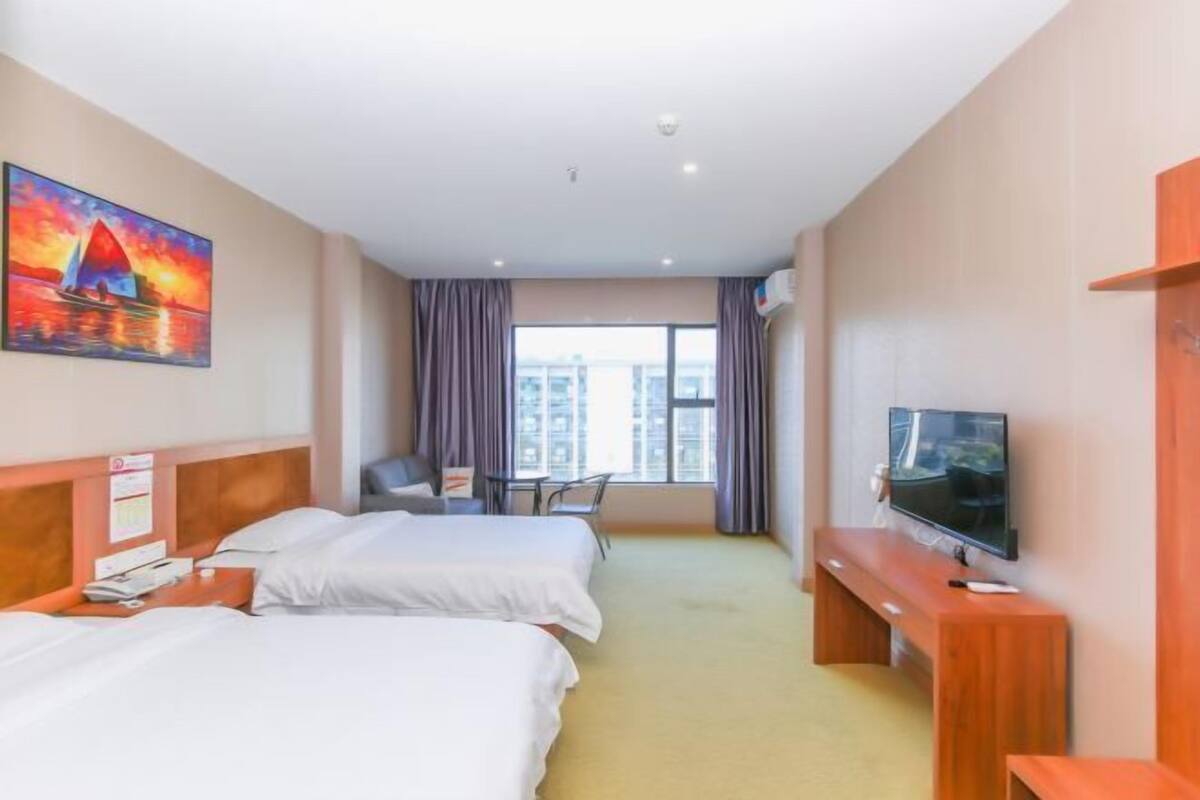 Ein Hotelzimmer mit zwei Betten, einem Fernseher, einem Schreibtisch und einem fensterbepflanzten Fenster.
