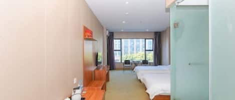 A hotel room with a bed, a desk, a chair, a TV, and a window with a view of buildings.