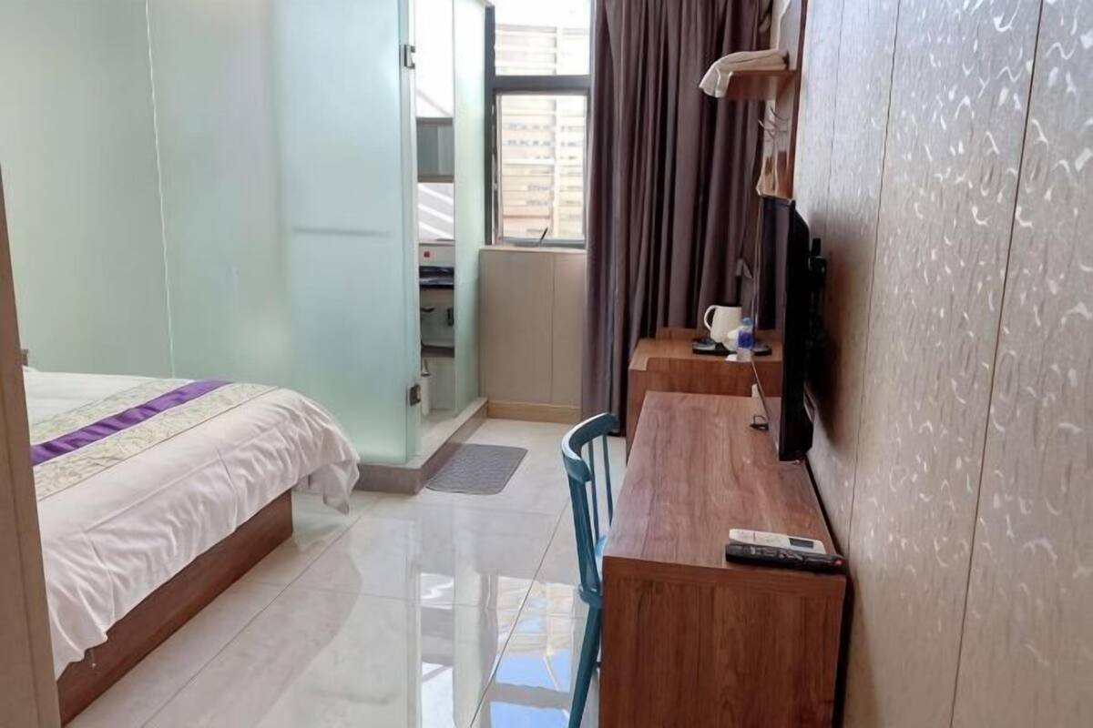 Ein Hotelzimmer mit Bett, Schreibtisch, Stuhl, Fernseher und einem fensterbepflanzten Fenster.