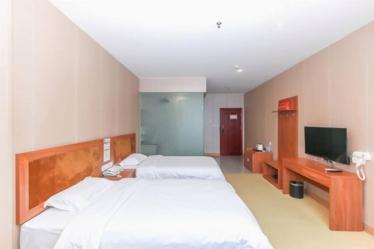 Ein Hotelzimmer mit zwei Betten, einem Fernseher, einem Schreibtisch und einem Papierkorb.