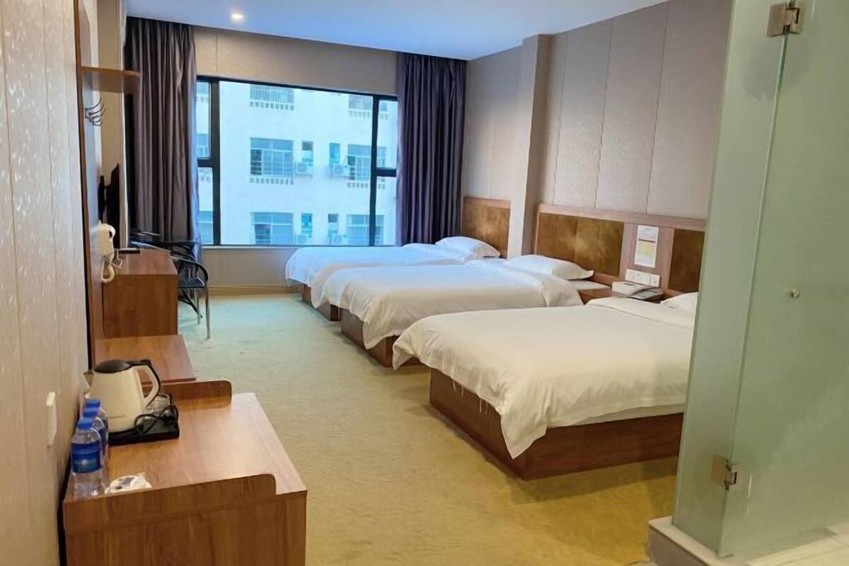 Ein Hotelzimmer mit zwei Betten, einem Schreibtisch mit Stuhl, einer Kaffeemaschine und Blick auf ein Gebäude durch das Fenster.
