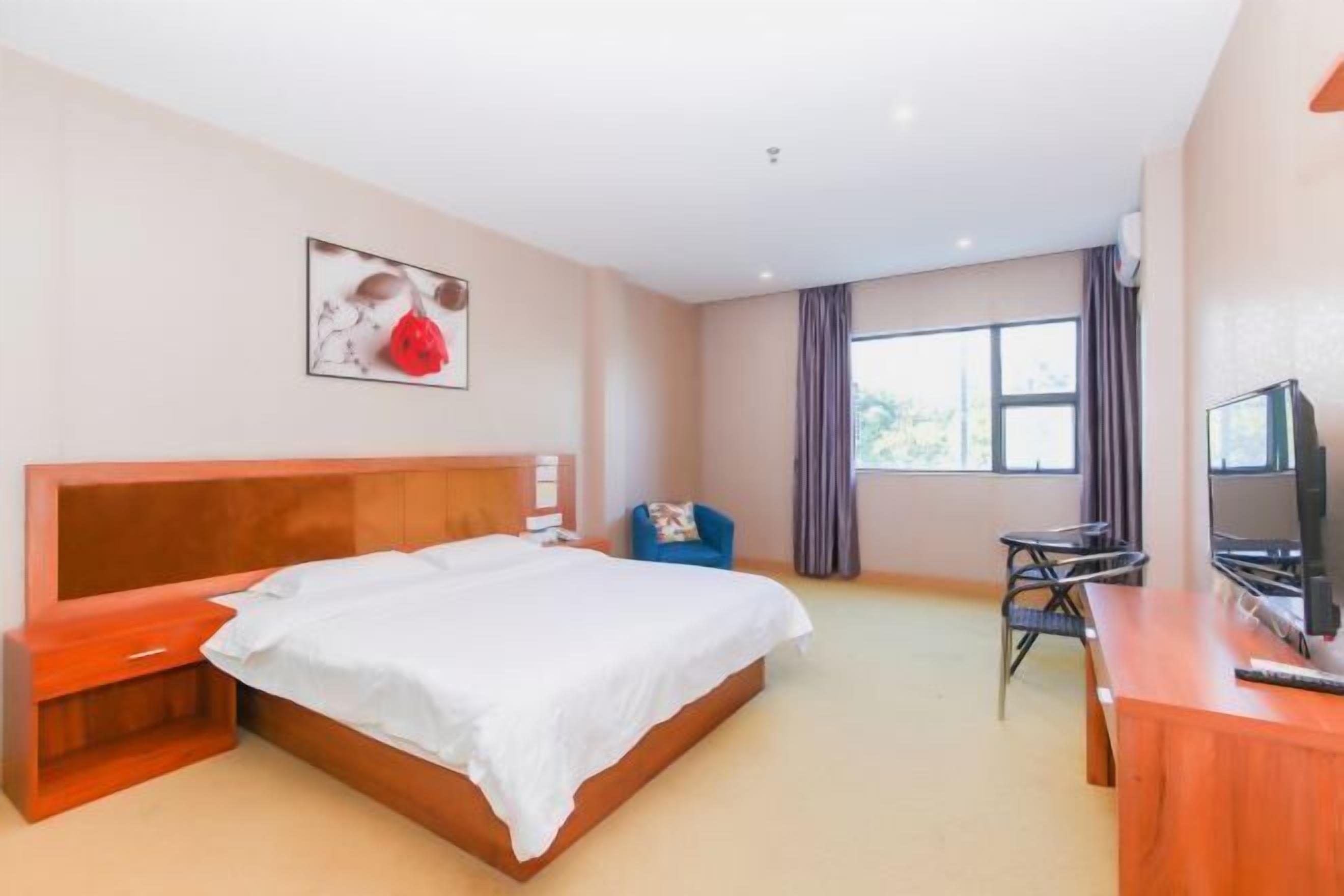 A hotel room with a large bed, a desk, a chair, a television, and a window with curtains.