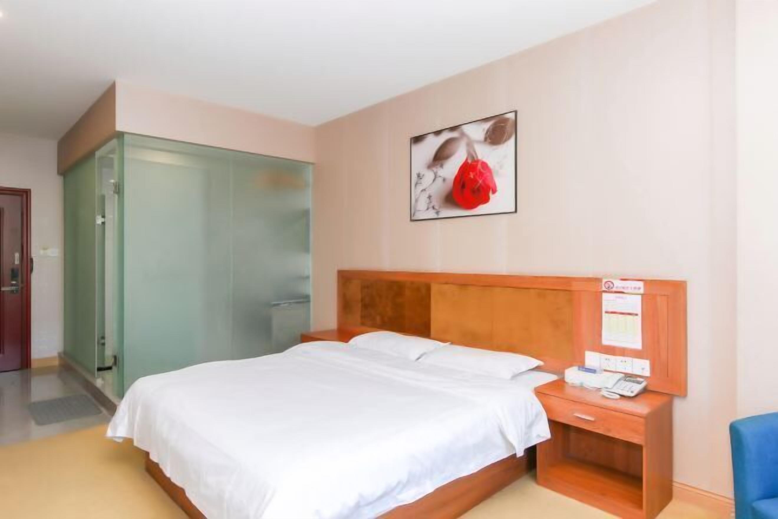 A hotel room with a bed, a wooden nightstand, a glass shower enclosure, and a wall-mounted telephone.