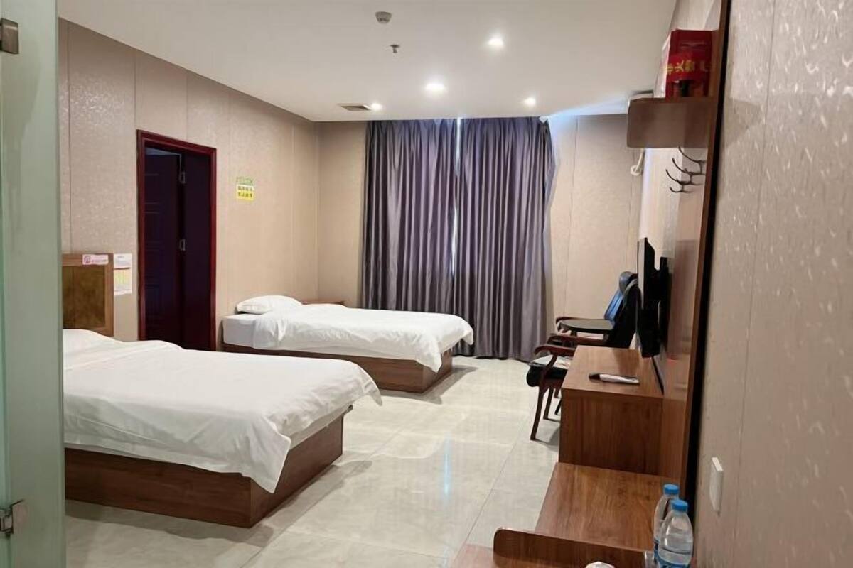 Ein Hotelzimmer mit zwei Betten, einem Schreibtisch, einem Sessel, einem Fernseher und einem Vorhang.