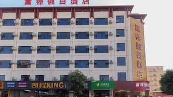 A multi-story hotel with a row of windows on each floor, a large yellow sign on the right side, and several storefronts at the ground level.