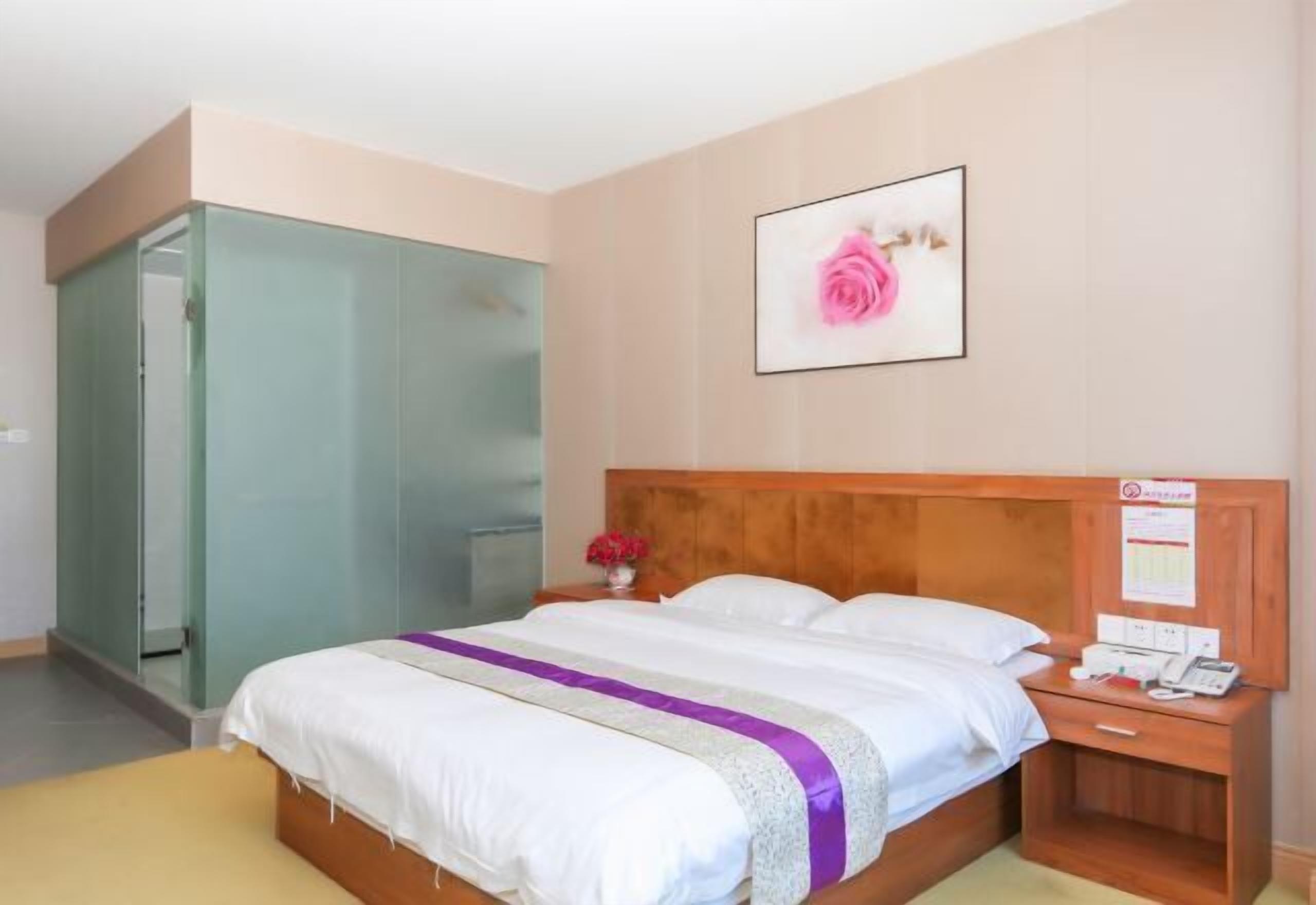 A hotel room with a bed, a nightstand with a phone, a wooden headboard, and a green wardrobe.