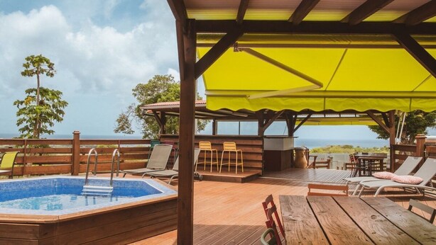 Eine Holzterrasse mit Whirlpool, Liegestühlen und einem gelben Sonnenschirm.