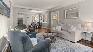 Ein modernes Wohnzimmer mit grauem Sofa, blauen Sesseln, einem Couchtisch und einem Essbereich im Hintergrund.