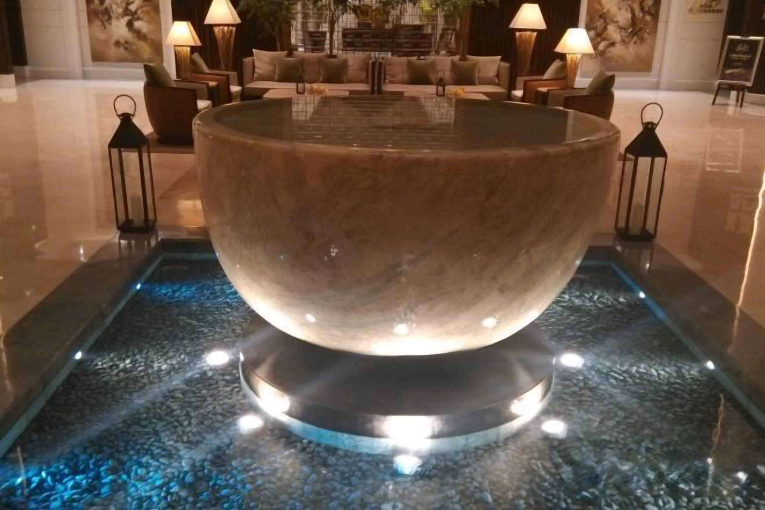Una amplia fuente iluminada en un vestíbulo, con asientos y una escalera al fondo.