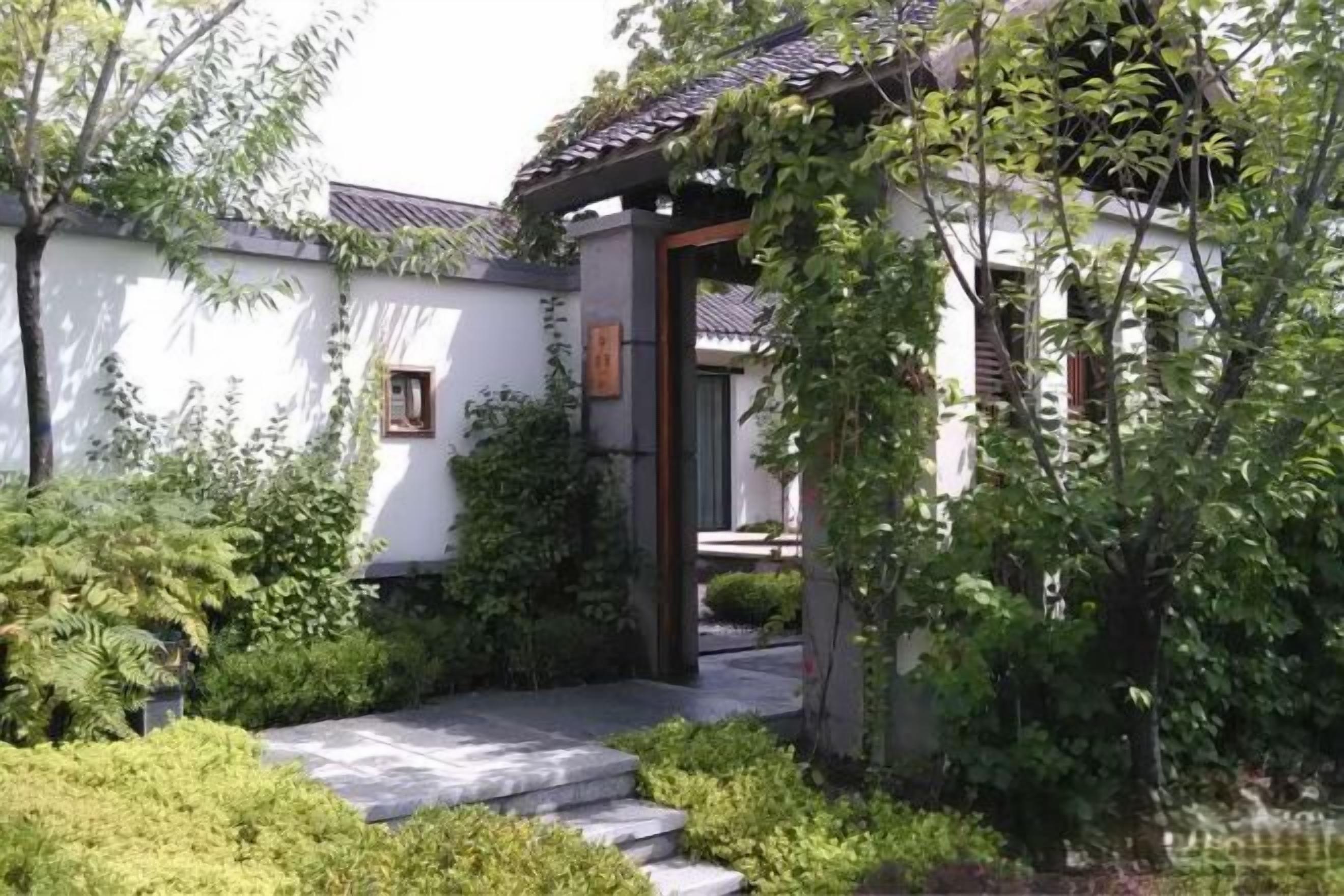 A traditional building with a tiled roof, a stone pathway leading to the entrance, and lush greenery surrounding the structure.