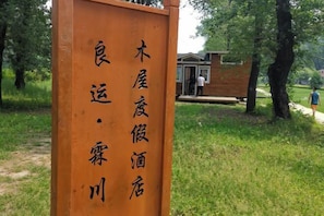 A wooden sign with Chinese characters, a wooden structure, and a grassy area with trees.
