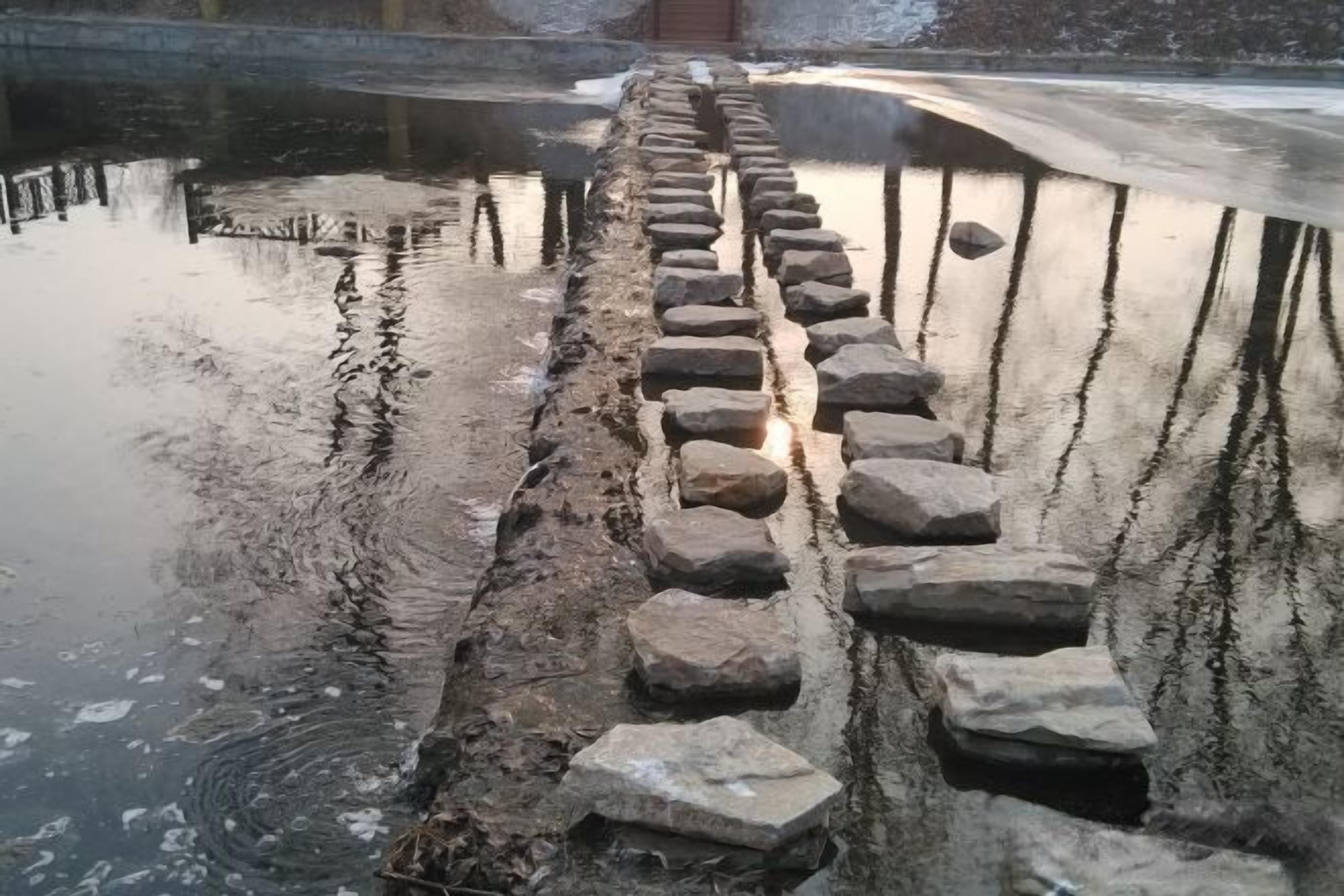 A stone pathway leading to a bridge over a body of water.