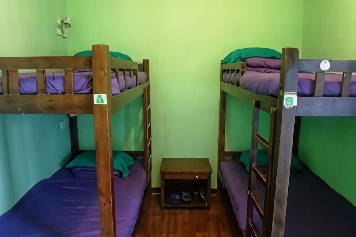 A room with two bunk beds, a small wooden table, and a shelf with shoes.