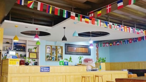 A restaurant interior with a wooden counter, bar stools, hanging flags, pendant lights, and a television screen. - Shiguanguyi Youth Inn (Guilin)