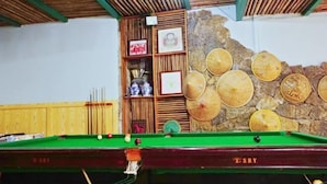 A billiards table with balls and cues, a wooden shelf with framed pictures, and a stone wall with woven hats. - Shiguanguyi Youth Inn (Guilin)